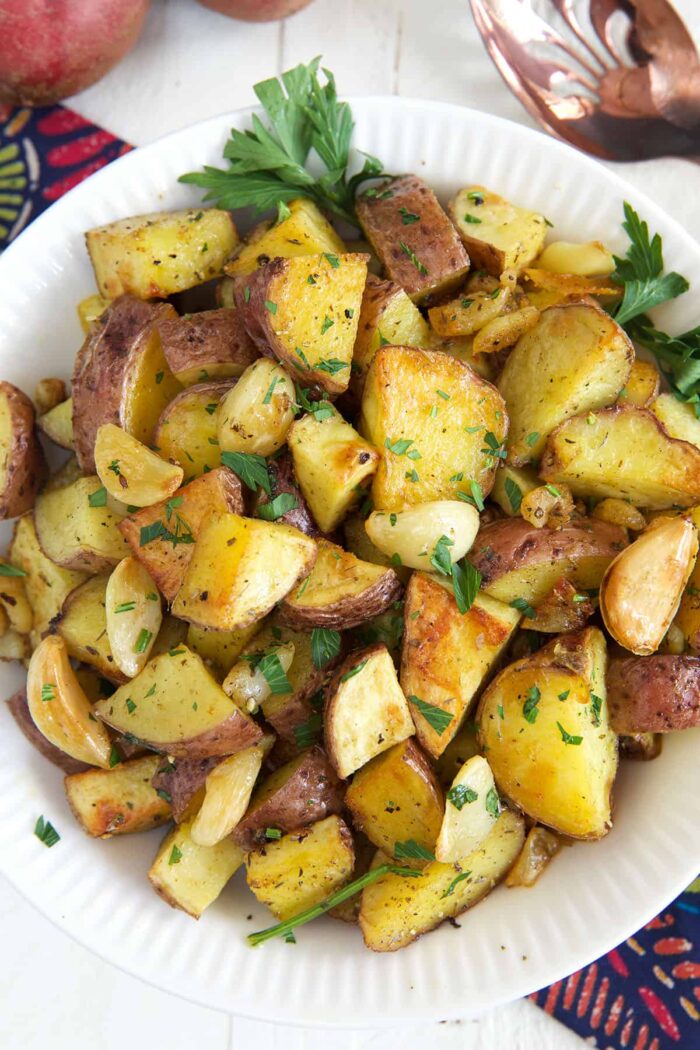 A bowl of roasted potatoes is garnished with parsley. 