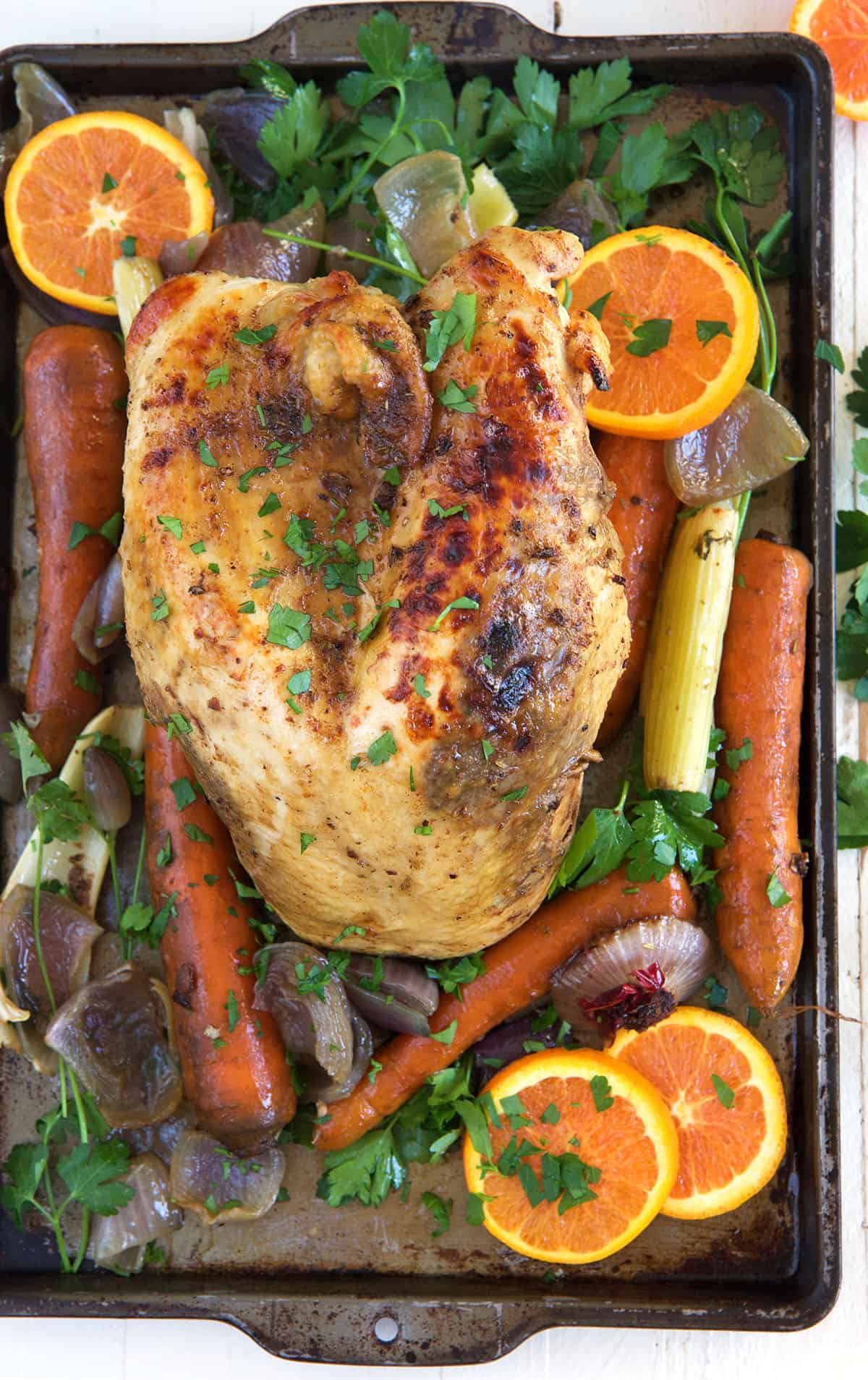 A cooked turkey breast is placed on a baking sheet with fruits and veggies.