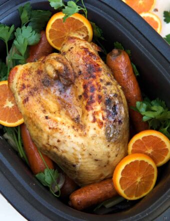 A cooked turkey breast is placed in a crockpot with veggies.