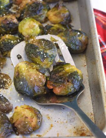 A spatula is lifting several cooked brussels sprouts from the tray.