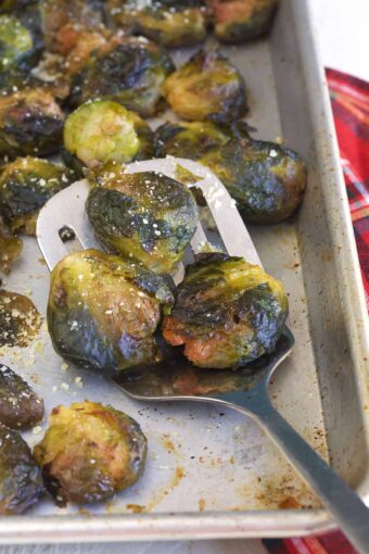 A spatula is lifting several cooked brussels sprouts from the tray.
