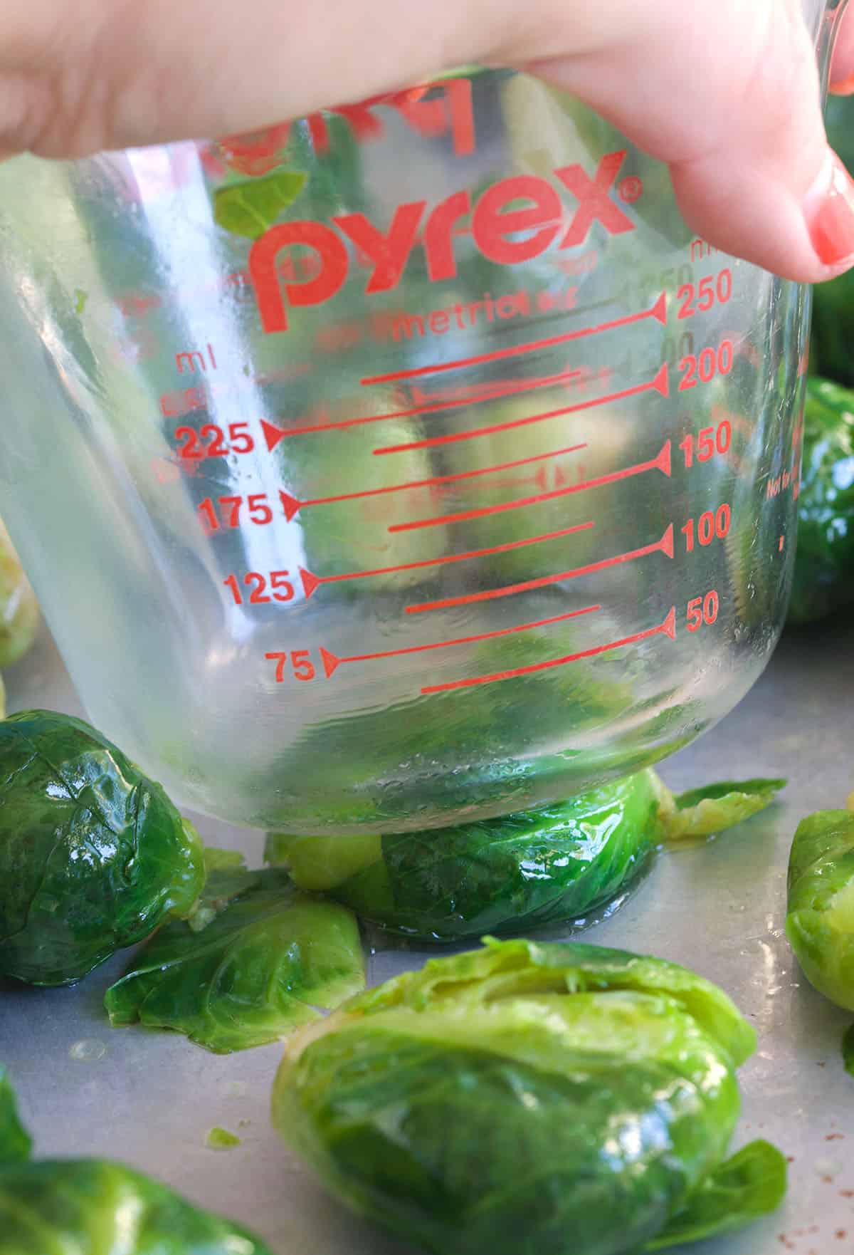A brussels sprout is being smashed by a measuring cup.
