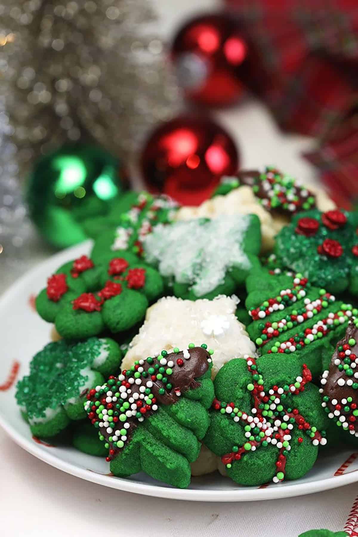 Spritz cookies on a plate with ornaments in the background.