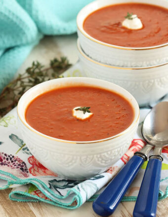 Two white bowls with tomato soup and a dollop of sour cream on top.