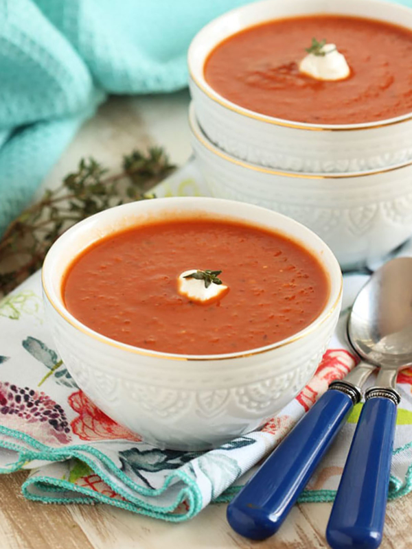 Two white bowls with tomato soup and a dollop of sour cream on top.