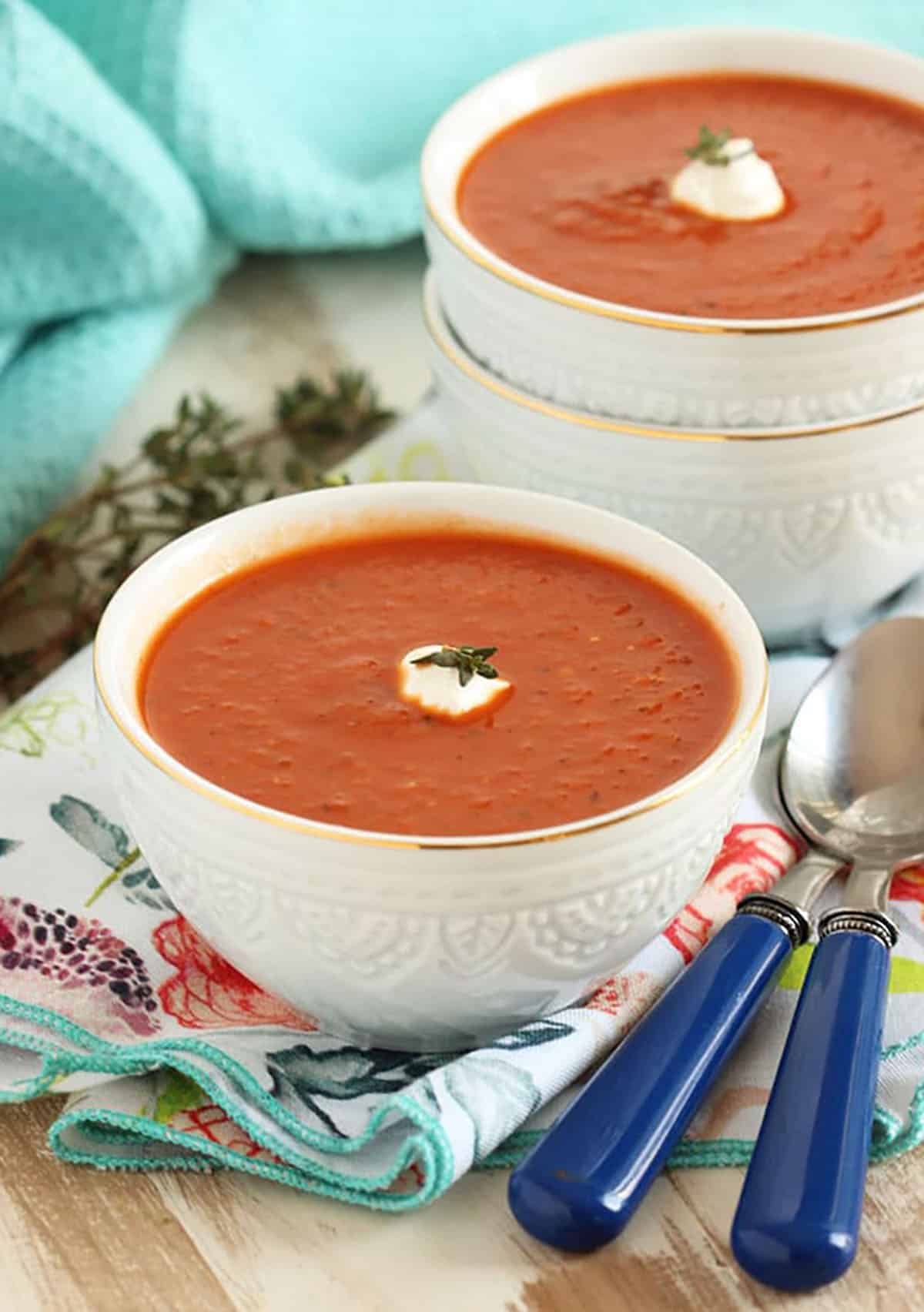 Two white bowls with tomato soup and a dollop of sour cream on top. 