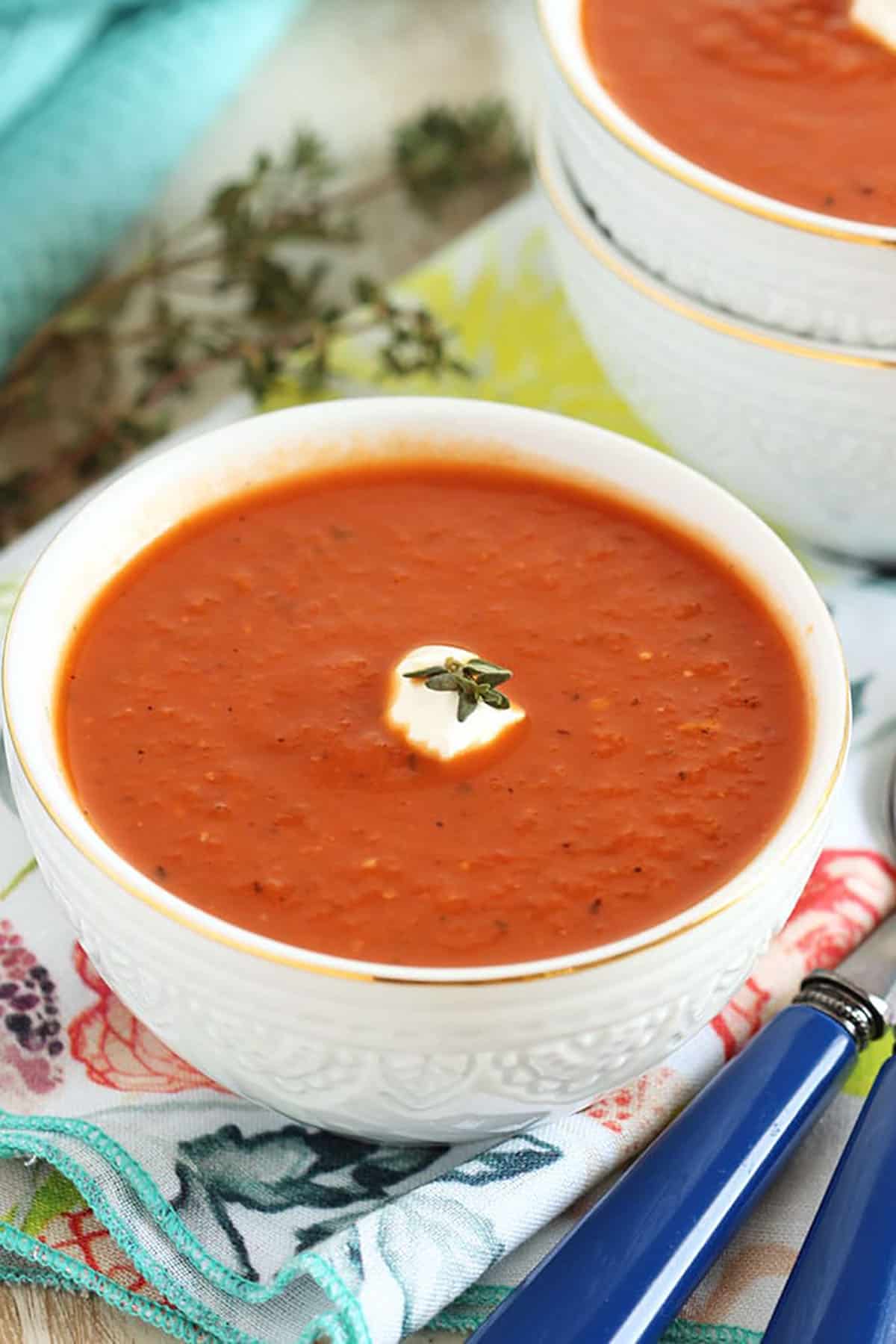 white bowl with tomato soup on a floral napkin with blue spoons