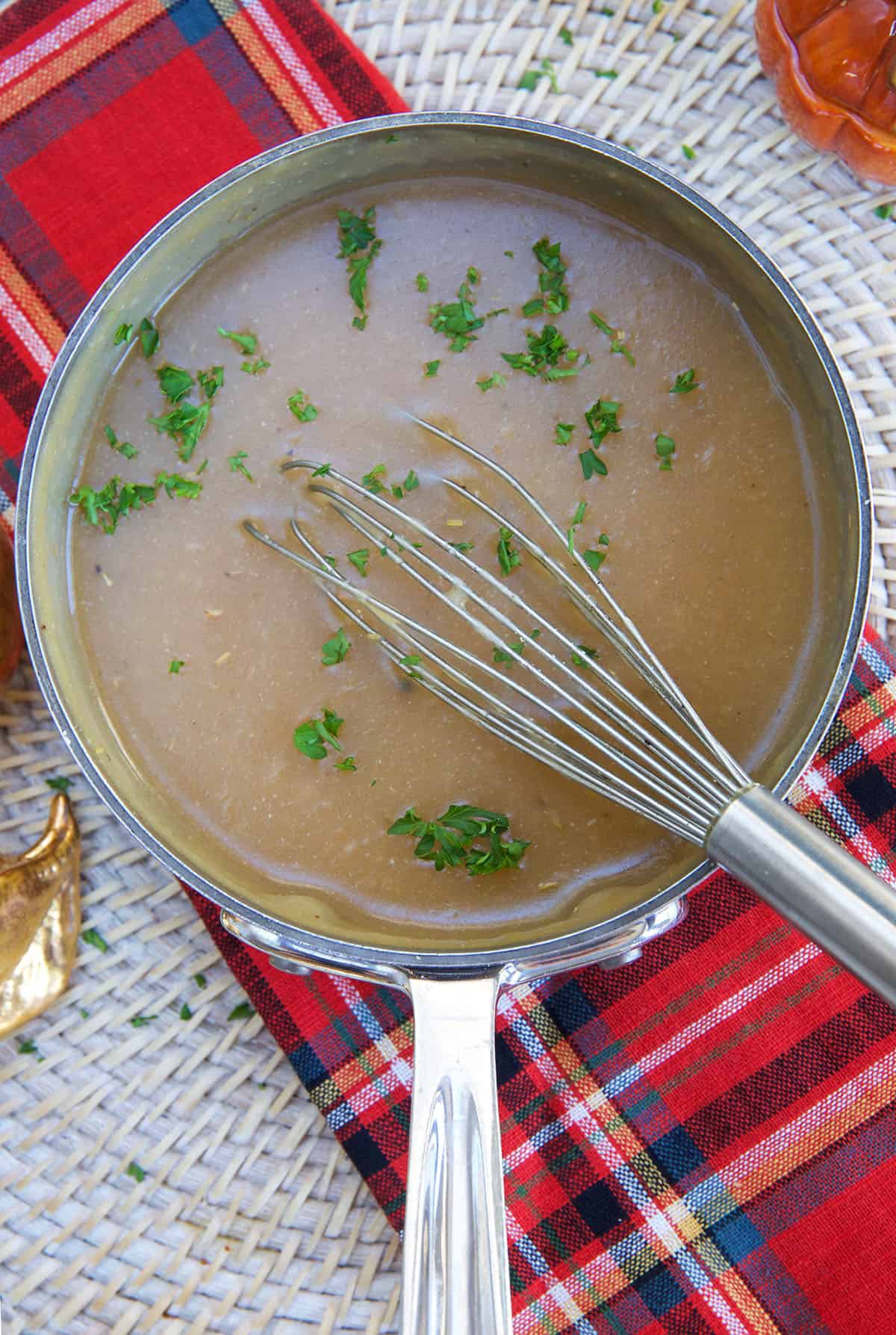 A whisk is placed in a pot full of gravy.