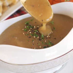 A spoon is drizzling gravy over a small white container.