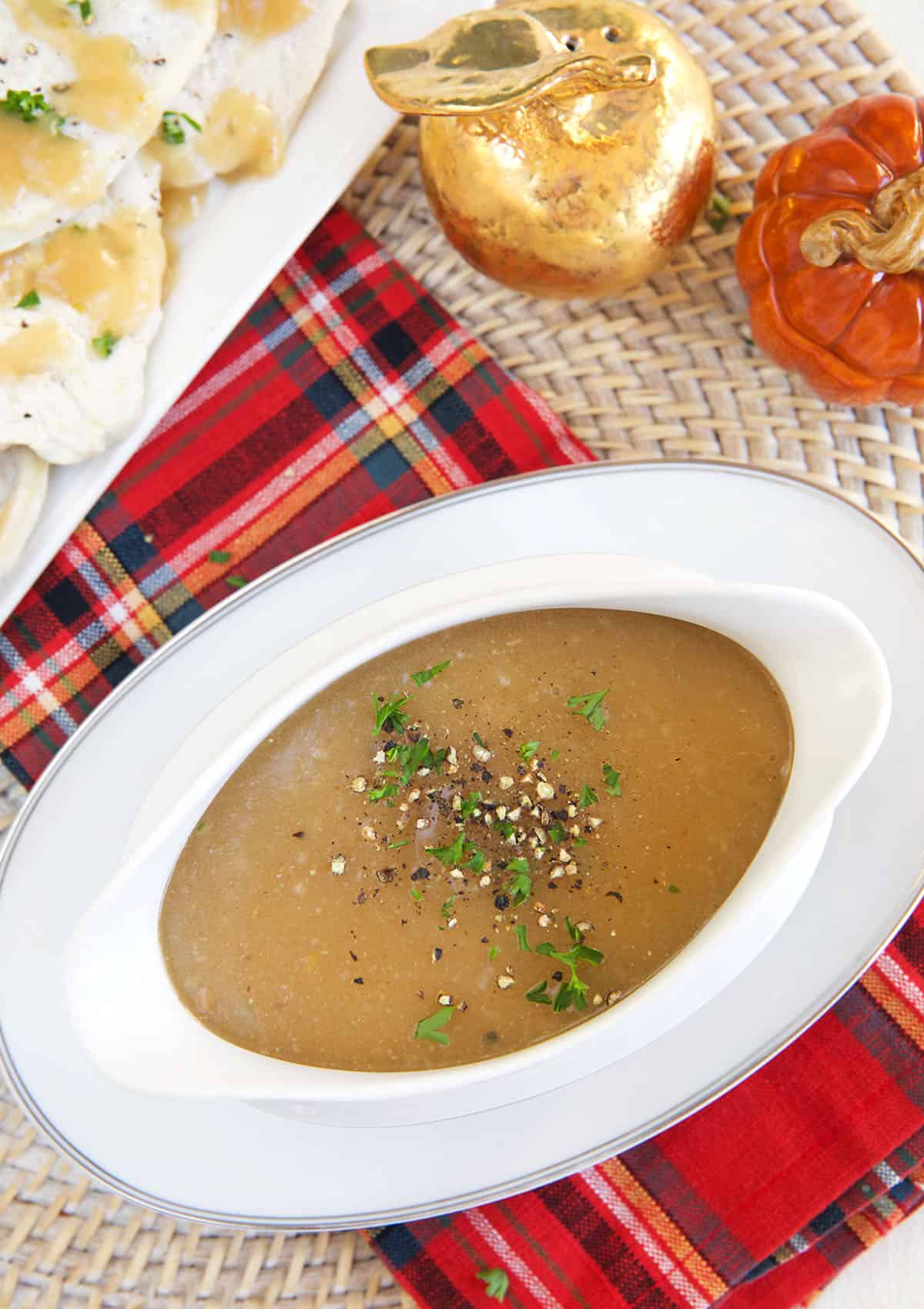 A white gravy boat is filled with garnished turkey gravy.
