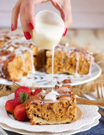 Slice of cinnamon roll casserole on a white plate with icing being drizzled on top