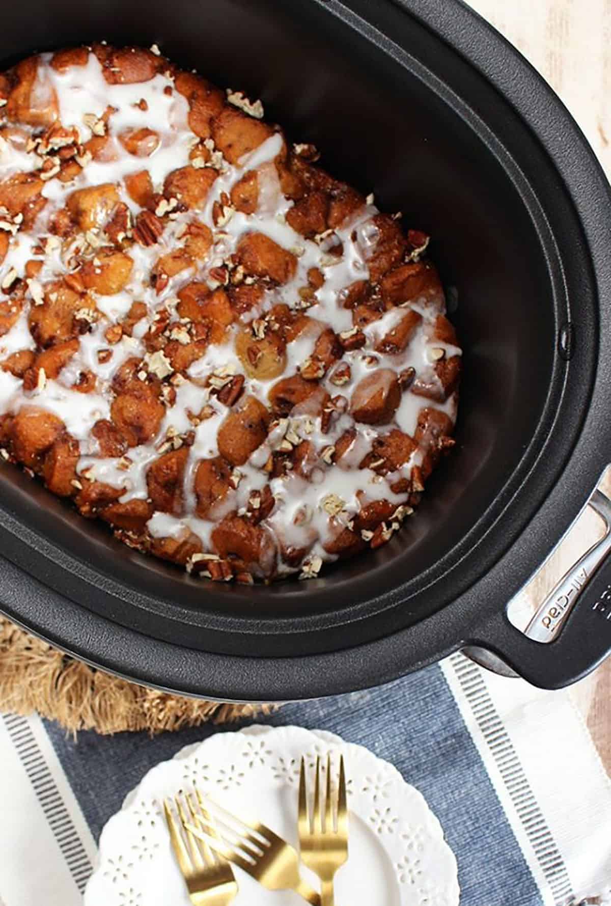cinnamon roll casserole in a slow cooker with a white plate next to it topped with two gold forks.