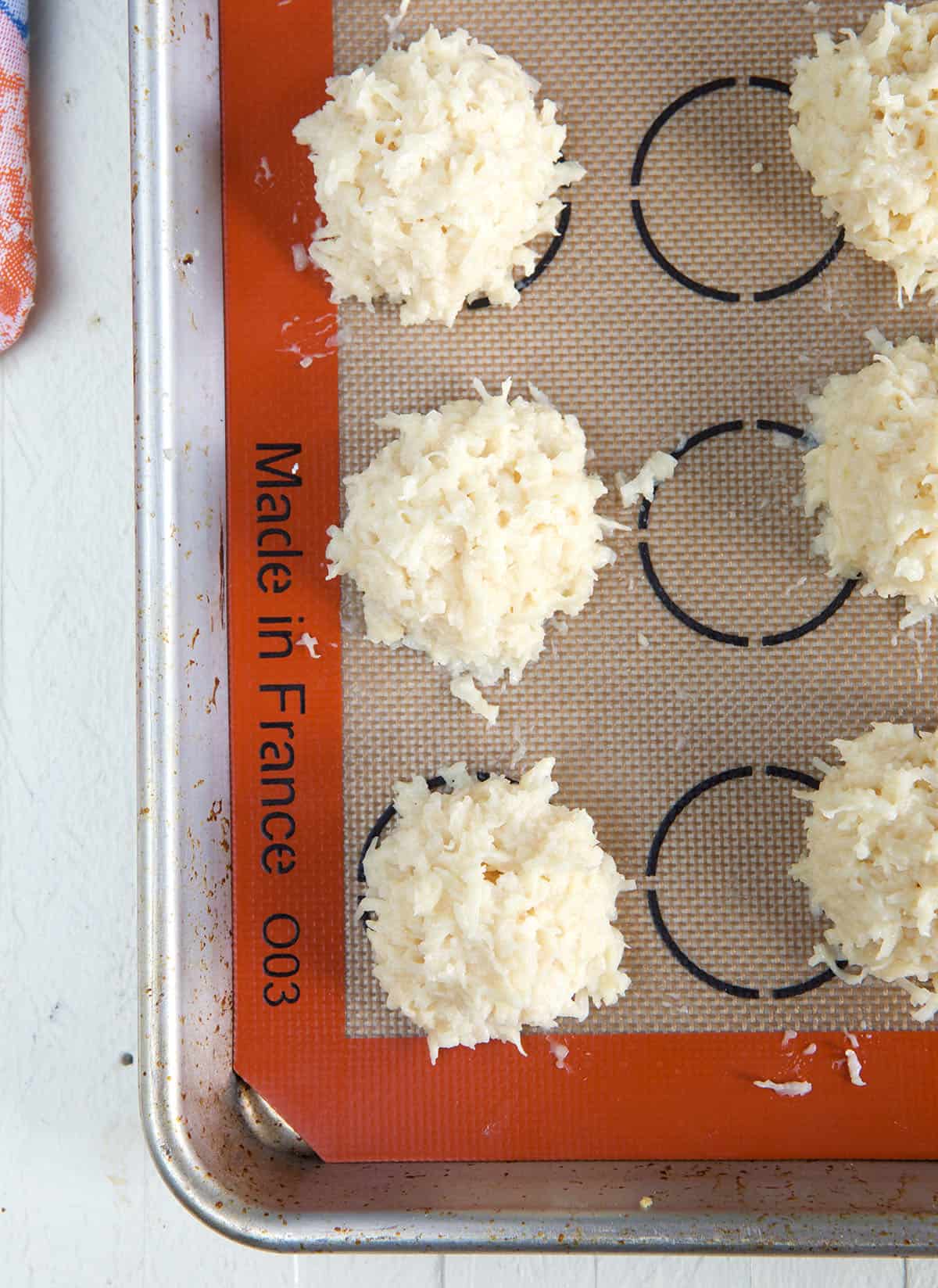 Uncooked macaroons are spread out on a baking sheet.