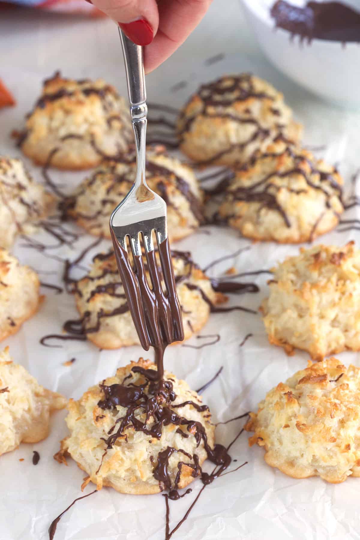 A fork is drizzling chocolate all over a macaroon. 