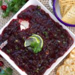A white square dish is filled with cranberry jalapeno dip.