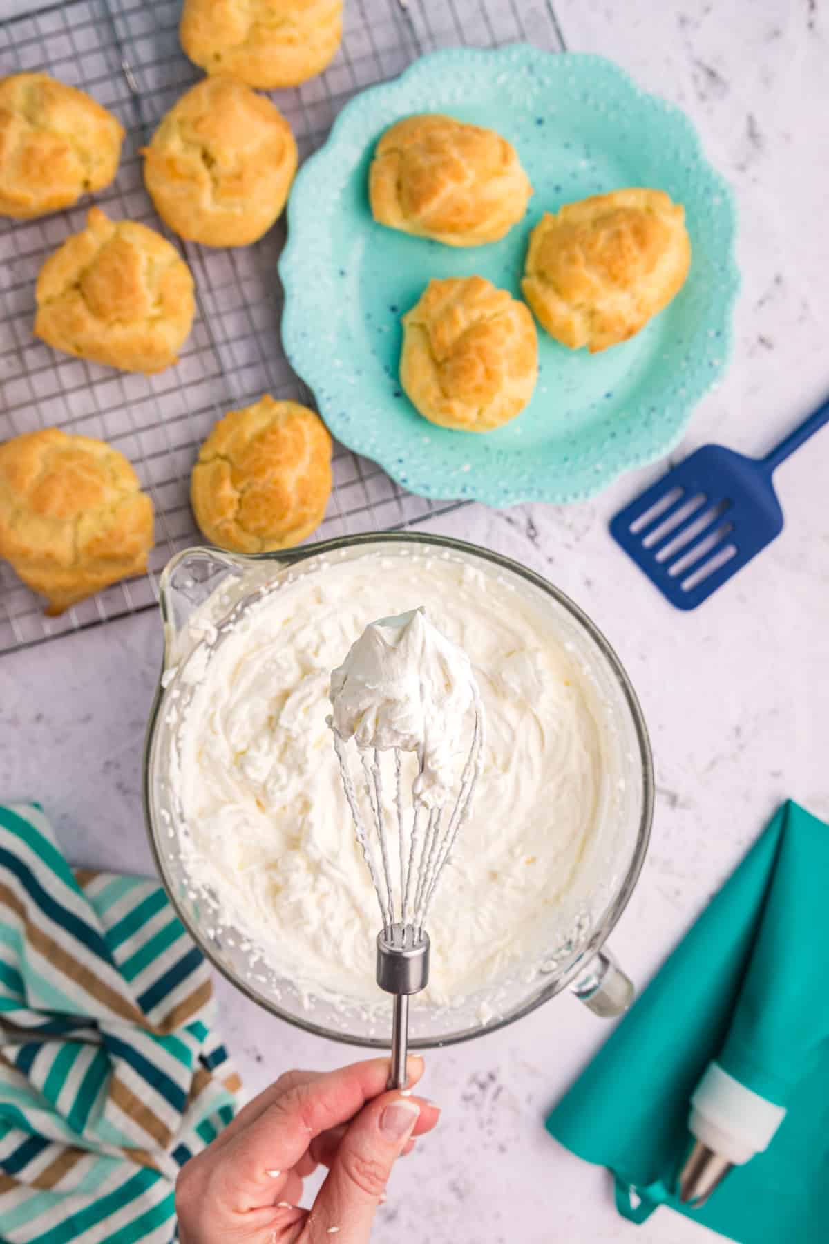 Whipped cream is being whisked in a bowl next to freshly baked puffs. 