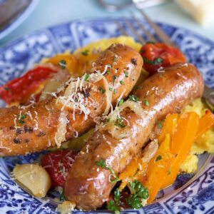 Two links of italian sausage and peppers with onions on a bed of polenta on a blue and white plate.