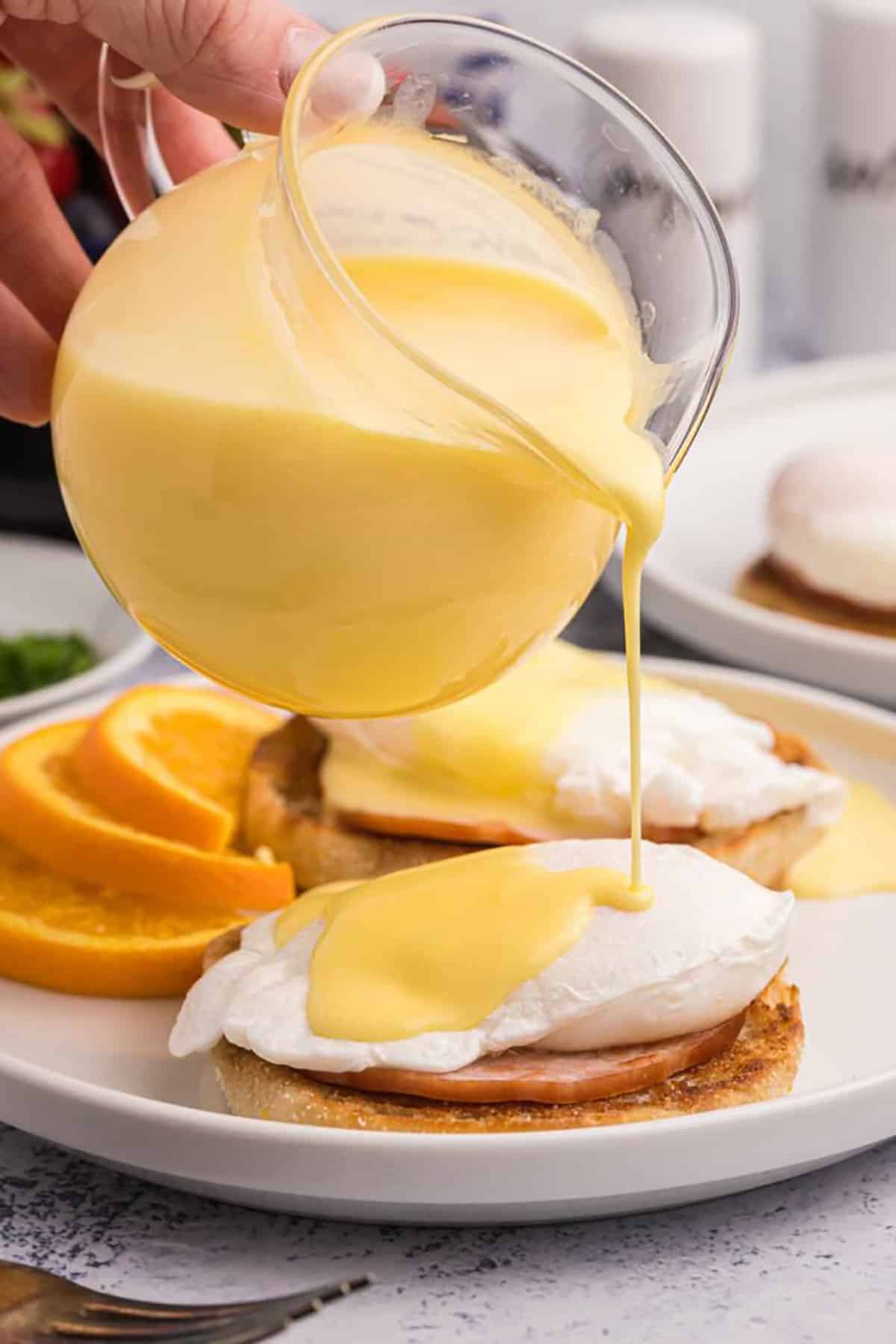 Hollandaise sauce is being poured over eggs benedict.