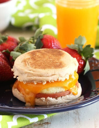 Egg McMuffin on a blue plate with strawberries and a glass of orange juice in the background.