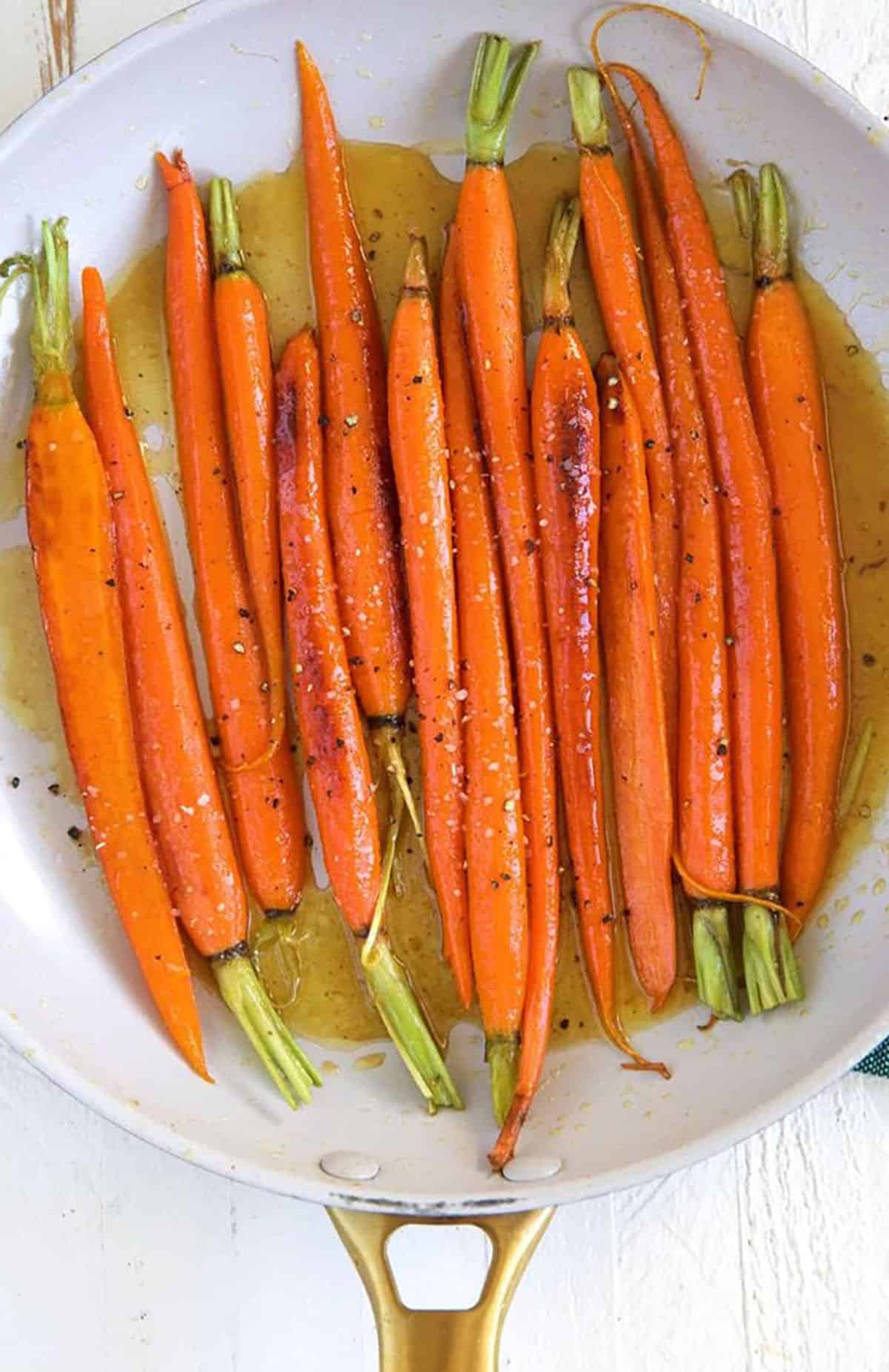 A white skillet is filled with glazed carrots.