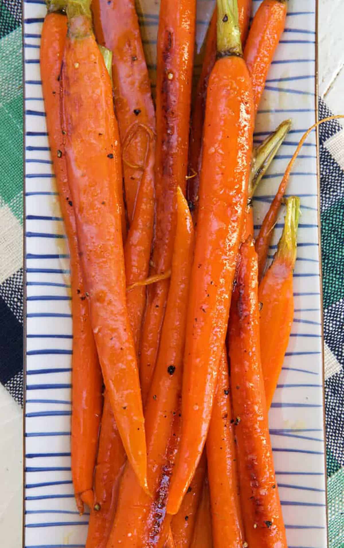 Honey glazed carrots are placed on a striped plate.