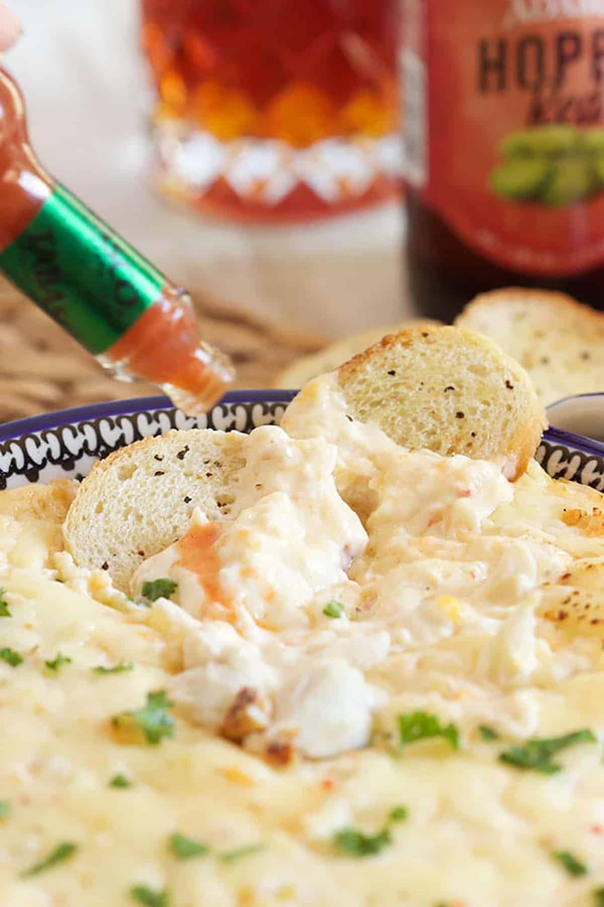 Hot Crab Dip in a baking dish with hot sauce being drizzled on top.