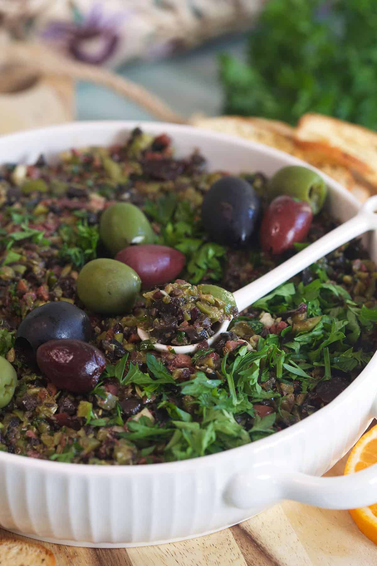 A white spoon is placed in a bowl of tapenade.