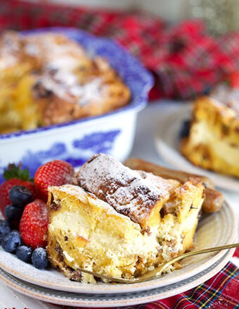 Cheesecake stuffed Panettone French Toast Casserole on a white plate with a gold fork and a plaid napkin.