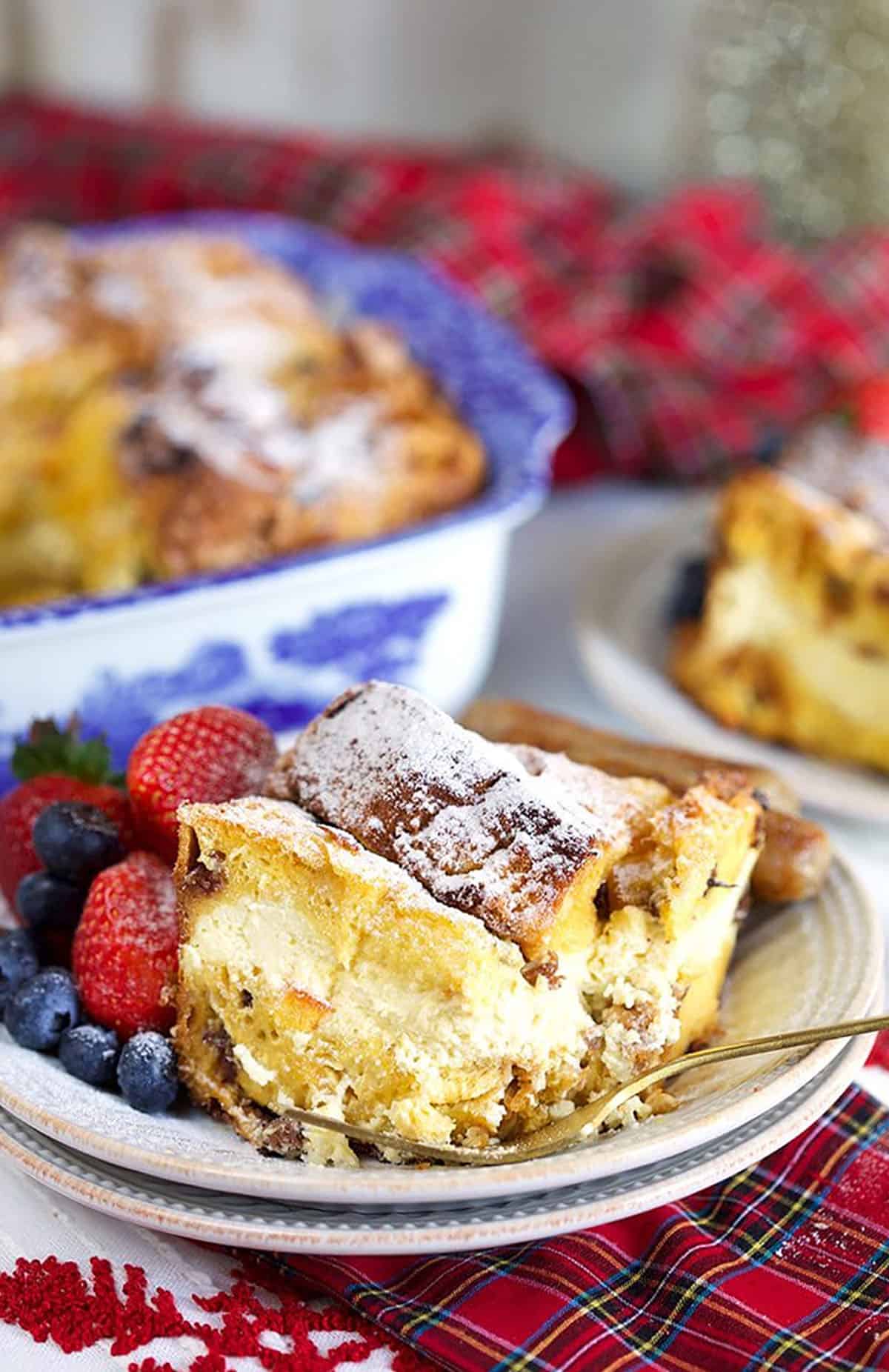 Cheesecake stuffed Panettone French Toast Casserole on a white plate with a gold fork and a plaid napkin.