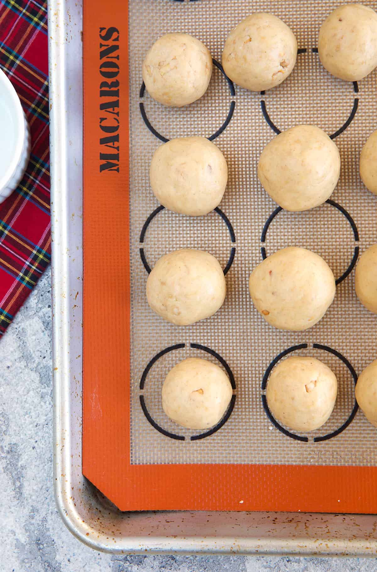 Peanut butter balls with no chocolate are spread out on a baking sheet.