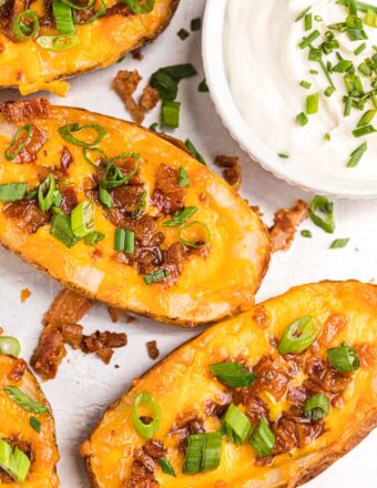 Several loaded potato skins are placed next to a small bowl of sour cream.