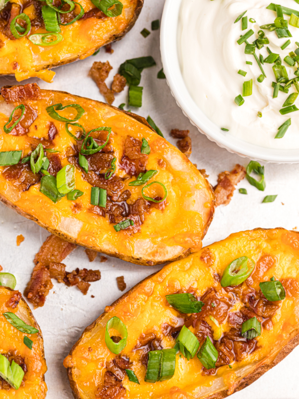 Several loaded potato skins are placed next to a small bowl of sour cream.