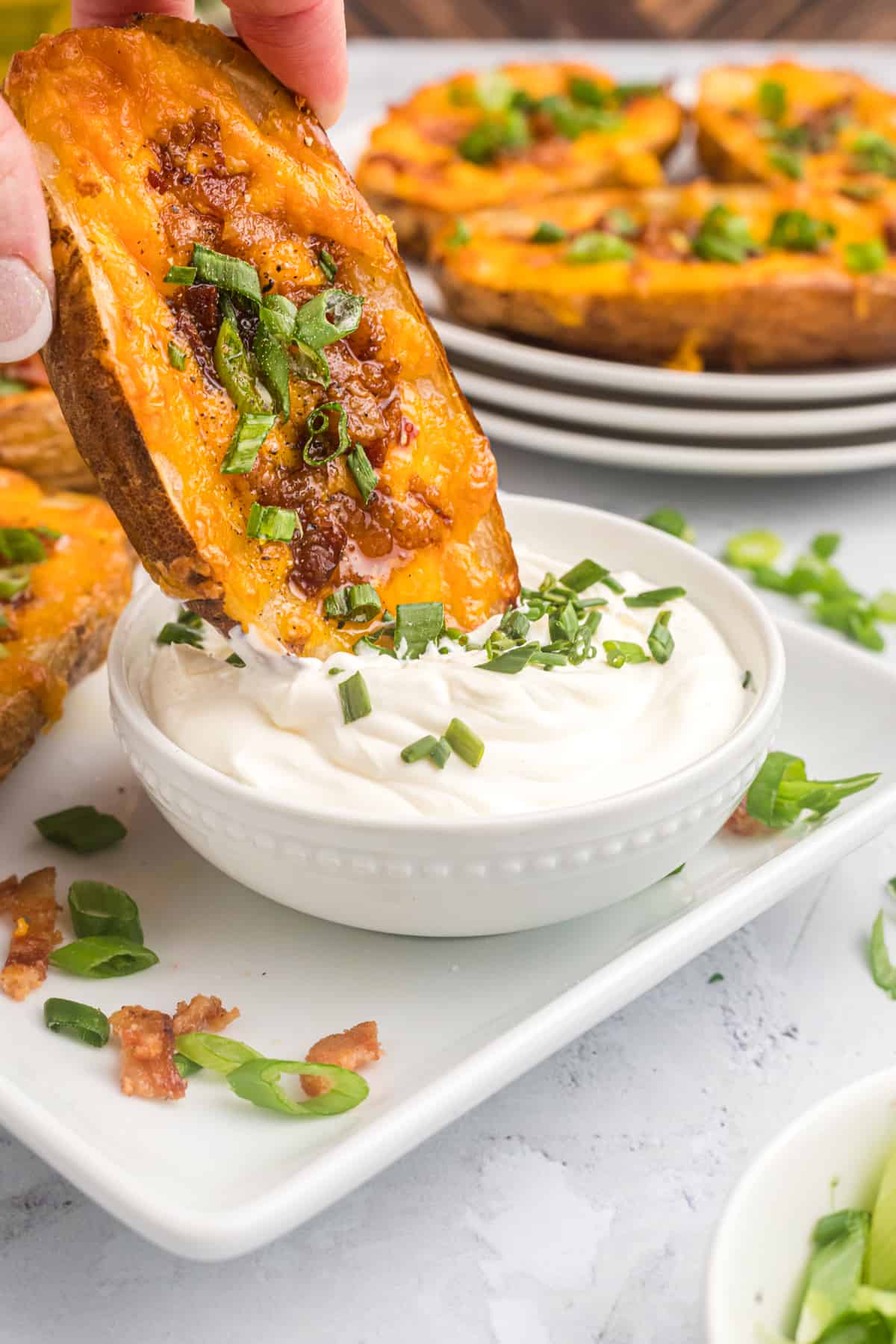 A loaded potato skin is being dipped into a bowl of sour cream.