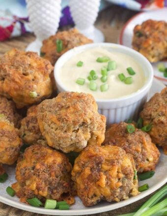 Sausage balls are placed on a plate next to a bowl filled with dipping sauce.