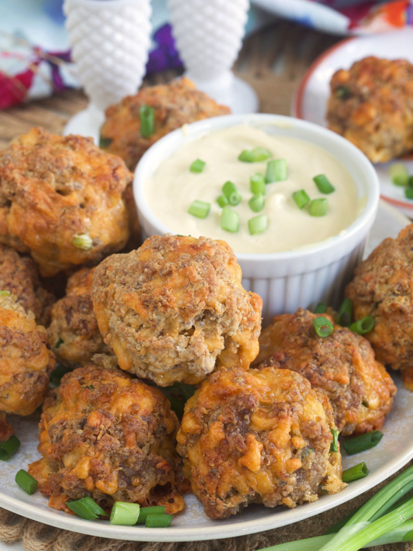 Sausage balls are placed on a plate next to a bowl filled with dipping sauce.