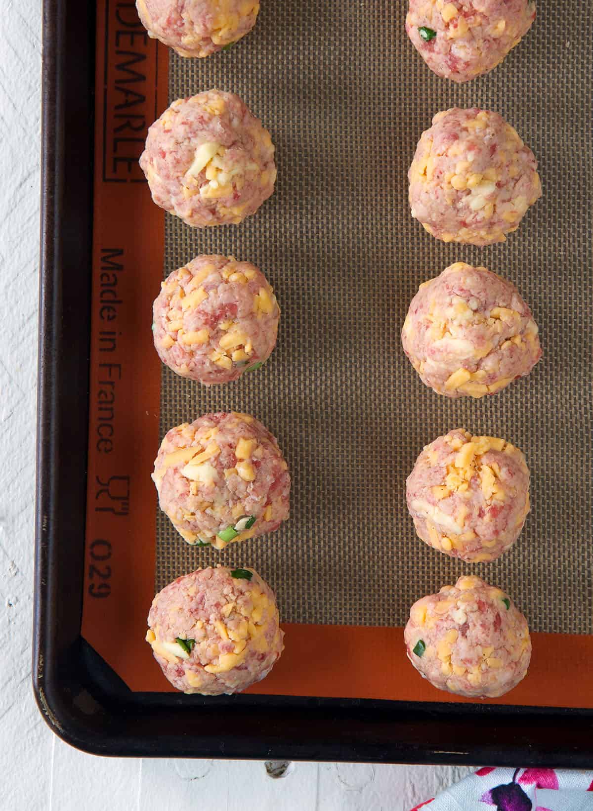 Raw sausage balls are placed on a baking sheet.