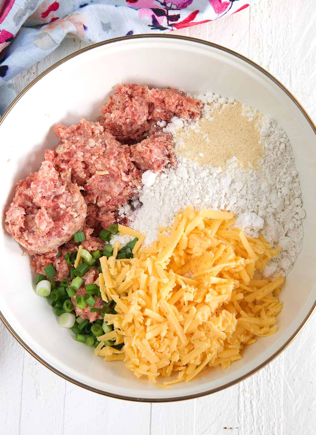 The ingredients for sausage balls are placed in a white mixing bowl.