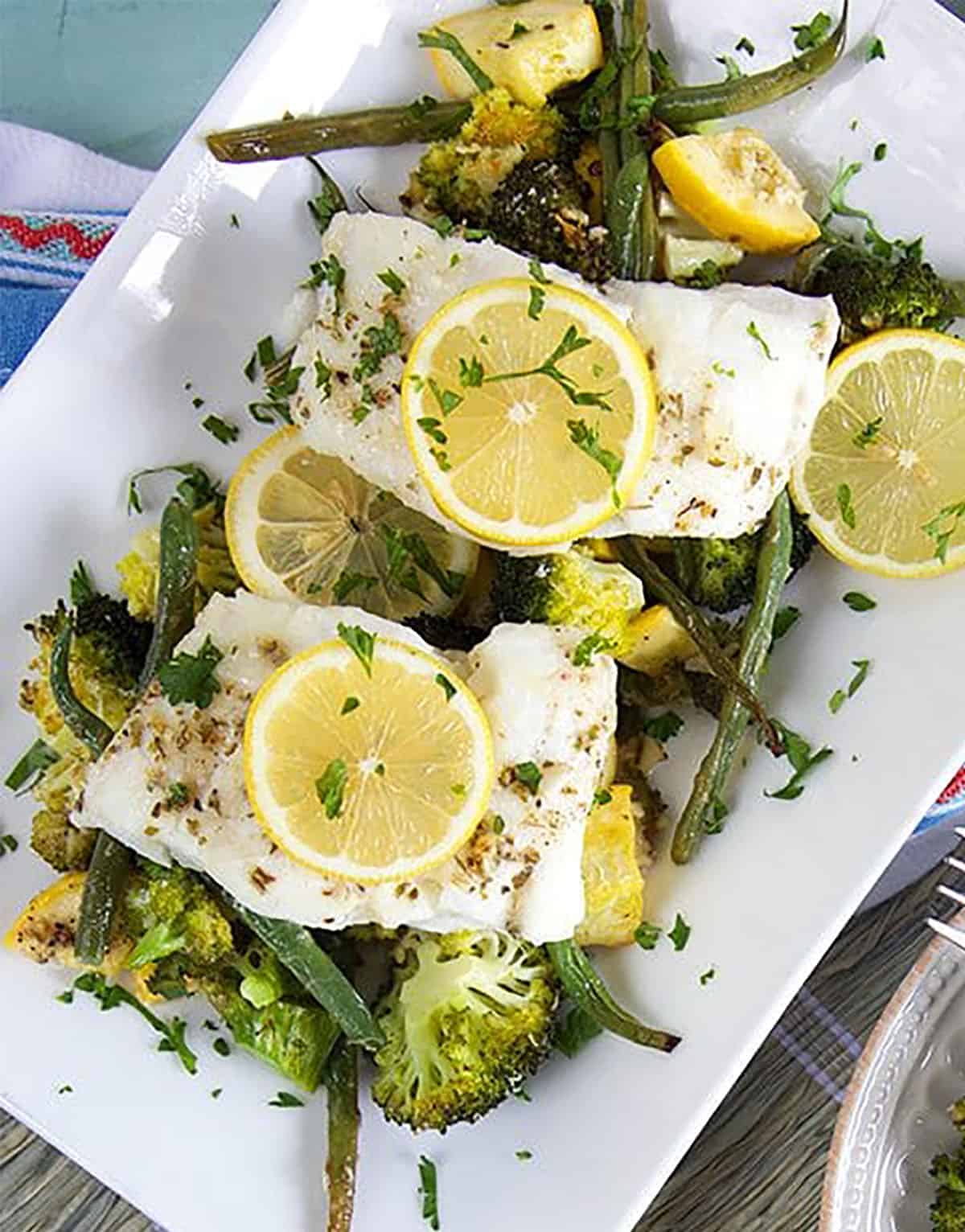 Cod filets with vegetables on a white serving platter.