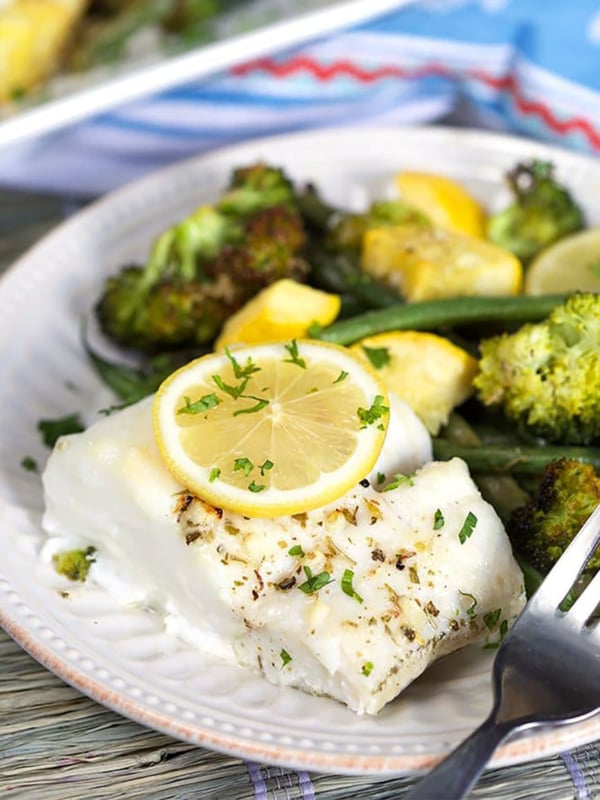 Baked Cod on a plate with a lemon slice on top.