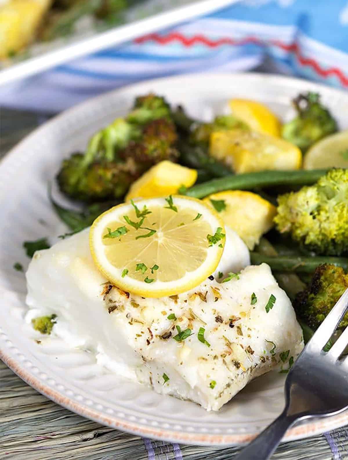 Baked Cod on a plate with a lemon slice on top.