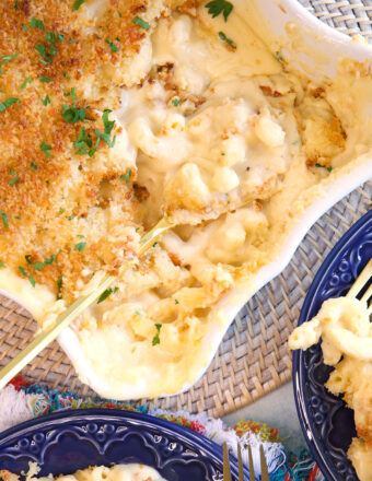 Five cheese baked Mac and cheese in a white casserole dish with a gold serving spoon in it.