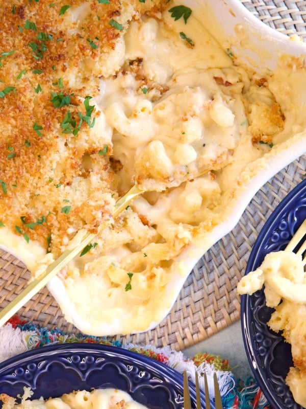 Five cheese baked Mac and cheese in a white casserole dish with a gold serving spoon in it.
