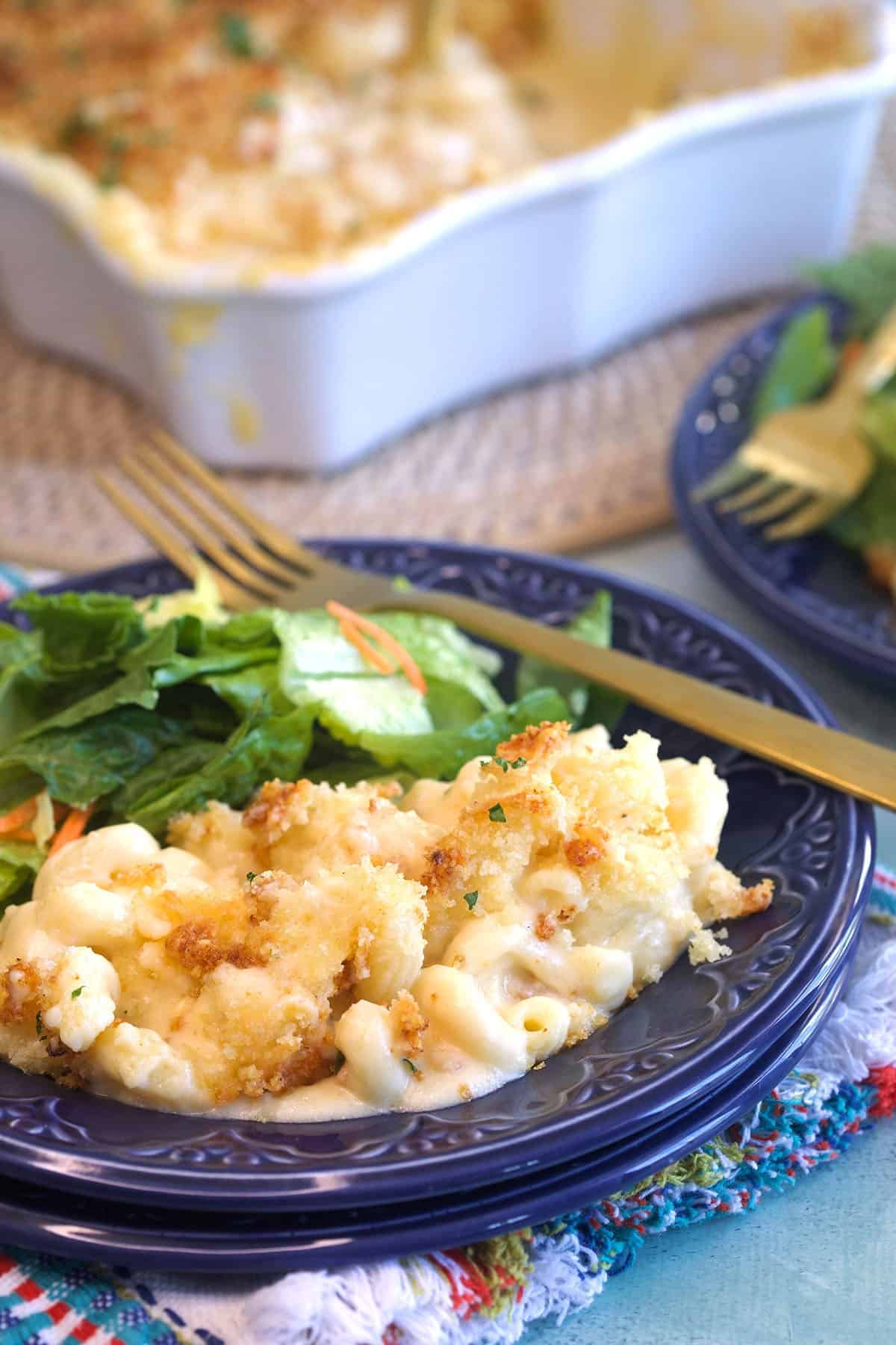 Baked macaroni and cheese on a blue plate with a salad and a gold fork.