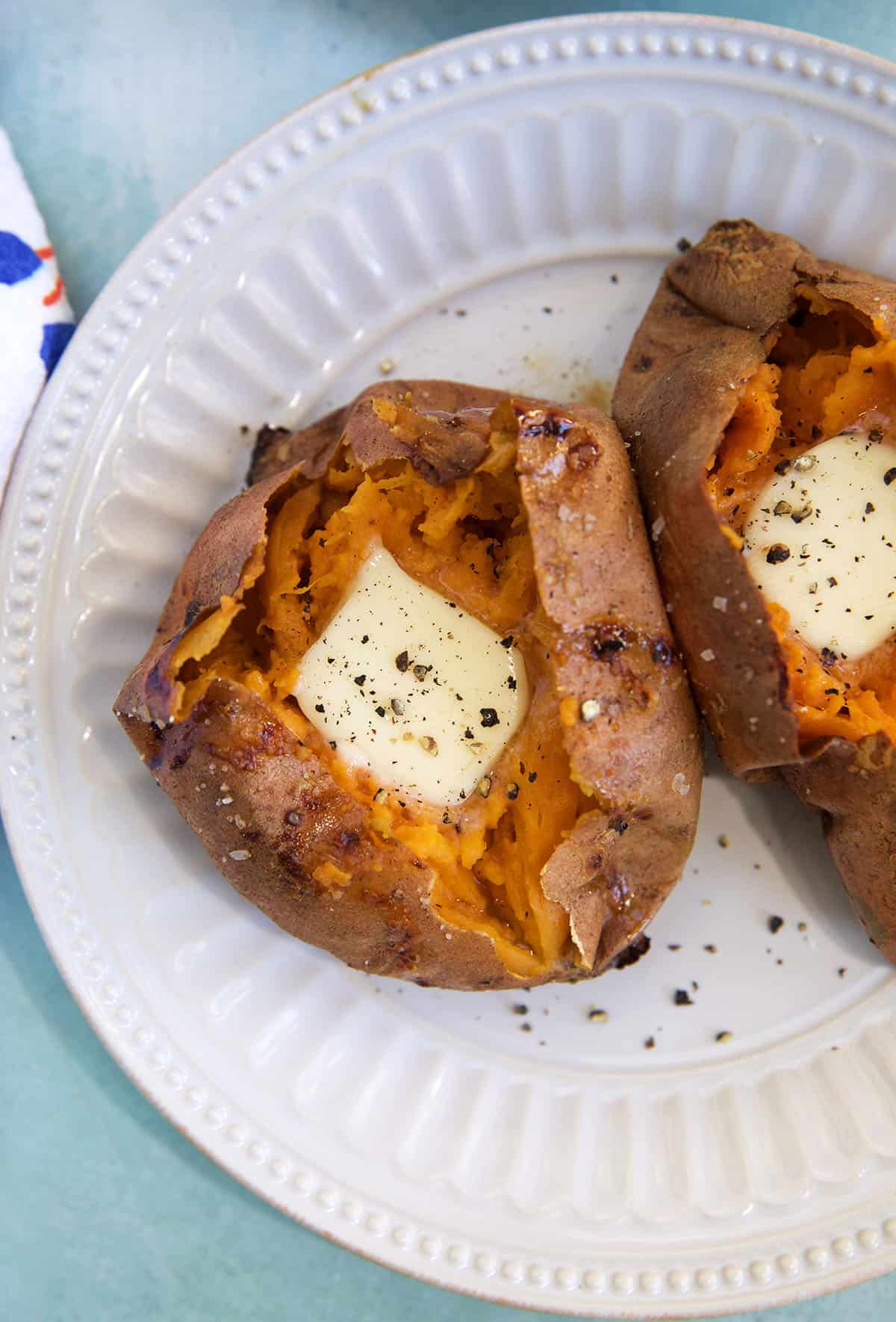 Two baked sweet potatoes are topped with butter and black pepper on a white plate.
