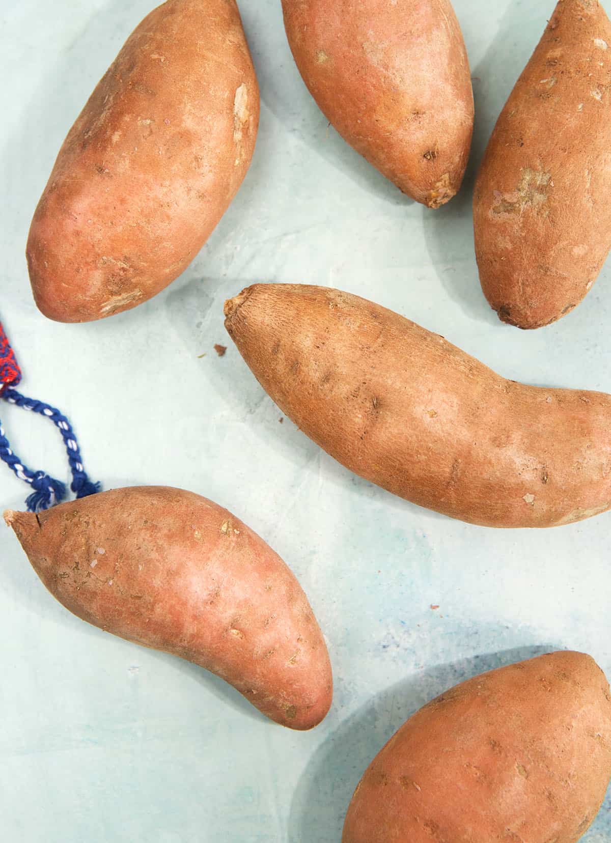 Several uncooked sweet potatoes are placed on a white surface.