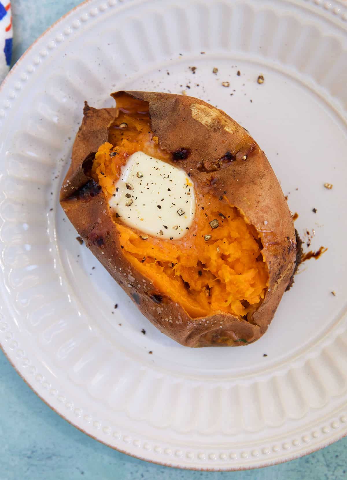 A cooked sweet potato is sliced and topped with butter and black pepper.