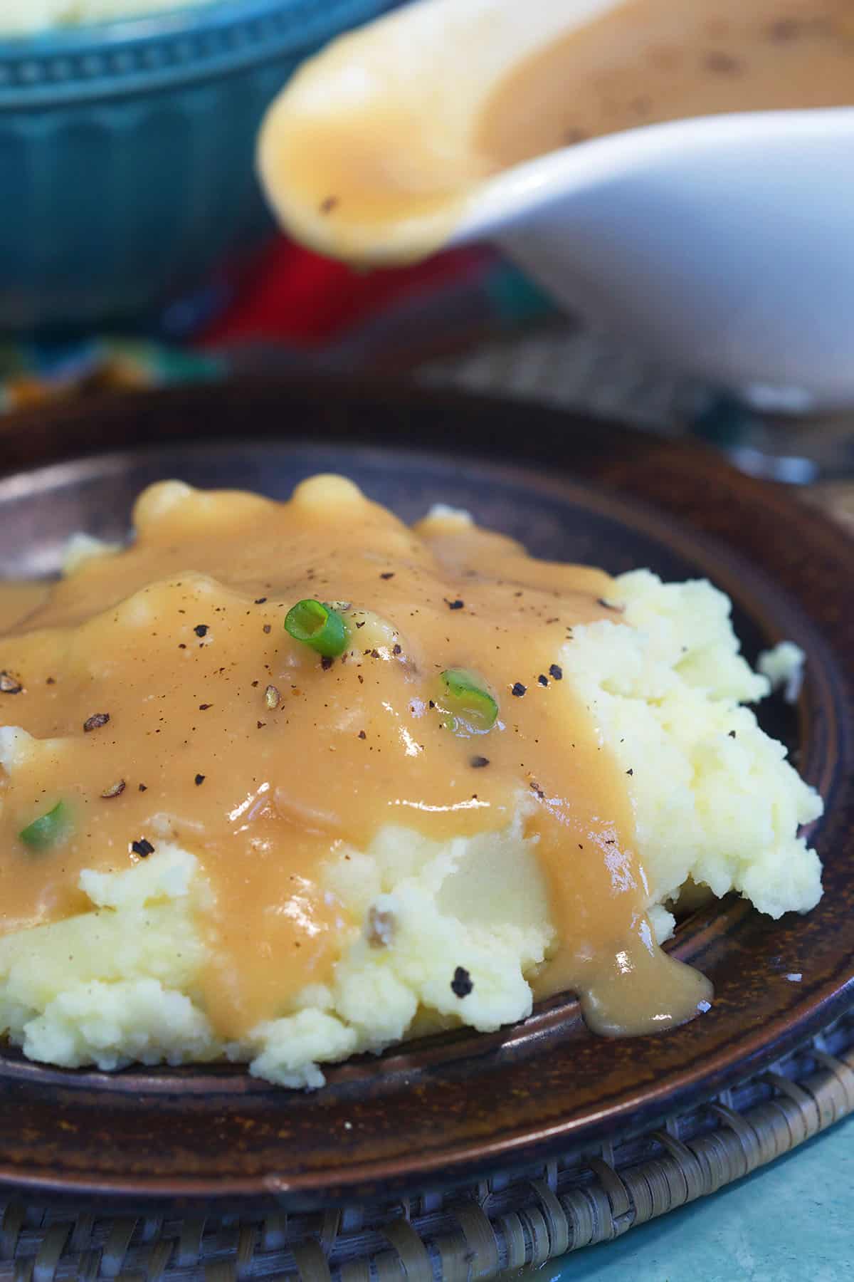 A serving of mashed potatoes with gravy is presented on a brown plate.