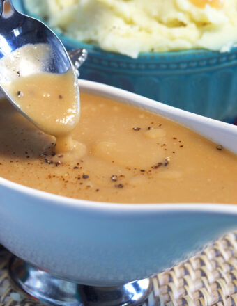 A spoon is drizzling brown gravy above a gravy boat.