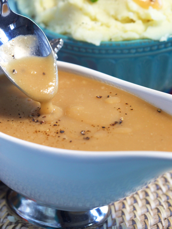 A spoon is drizzling brown gravy above a gravy boat.
