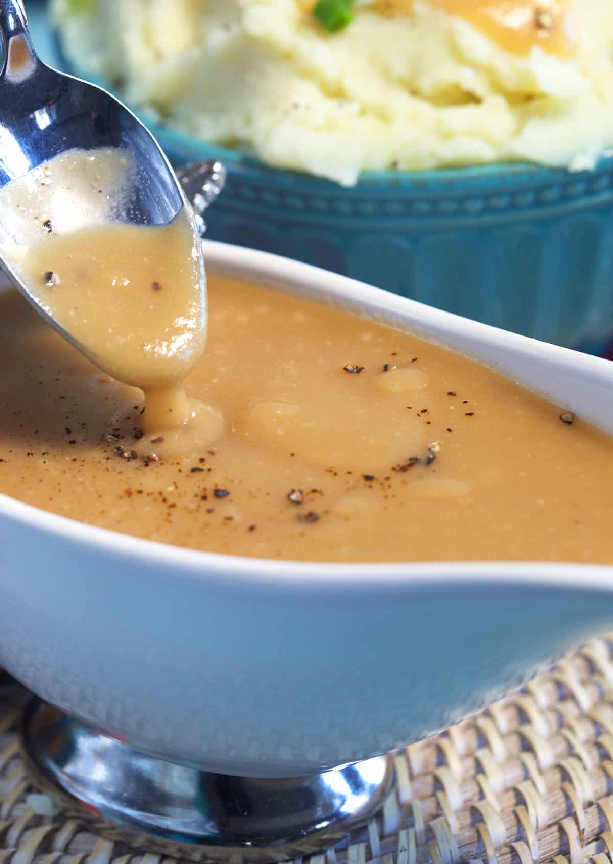 A spoon is drizzling brown gravy above a gravy boat.